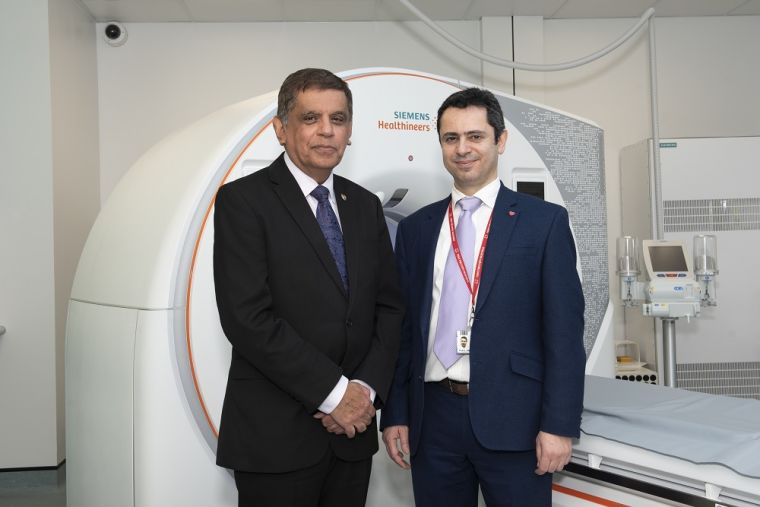 Two men in suits standing in front of ring-shaped medical imaging equipment.