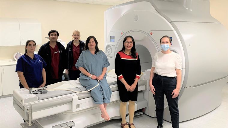 Group of people, one in hospital gown, in front of MRI scanner.