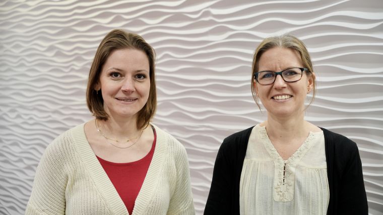 Two women standing in front of a white textured wall.
